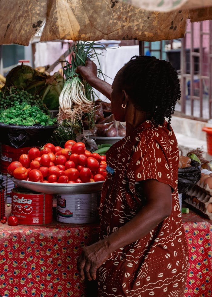 gallery-4 Woman shopping at a vibrant African market stall filled with fresh produce.