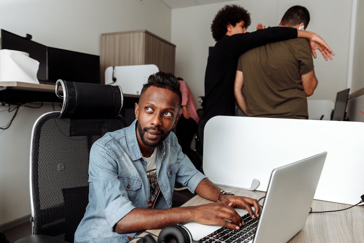 why-choose-us Young man working on a laptop in a modern collaborative office environment.