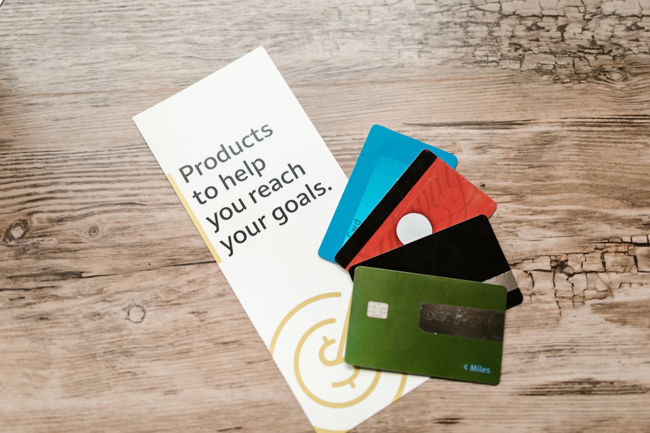 hero-img-01 Assorted credit cards on a wooden table next to a leaflet with motivational text about financial goals.